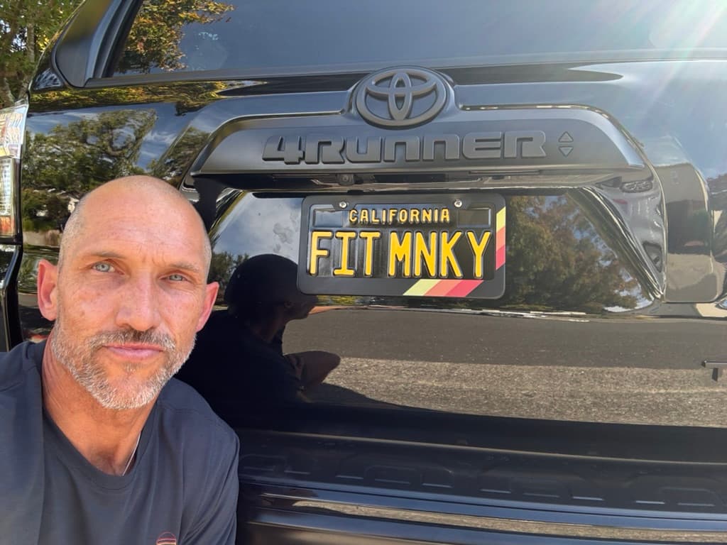 Chris Schuhmacher, founder of Fitness Monkey, beside his FIT MNKY license plate